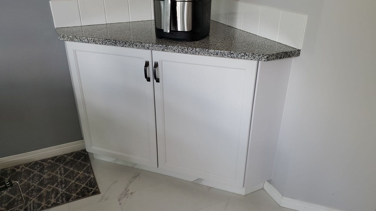 Light grey corner cabinetry with black hardware and speckled countertop